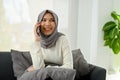 Cheerful Asian Muslim woman enjoys talking on the phone with her friend in her living room Royalty Free Stock Photo