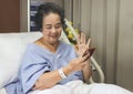 Cheerful  Asian senior  female patient  sitting  in hospital bed,  smiling and looking at mobile phone, video calling  and waving Royalty Free Stock Photo