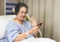 Cheerful  Asian senior  female patient  sitting  in hospital bed,  smiling and looking at mobile phone, video calling  and waving Royalty Free Stock Photo