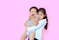 Cheerful asian sister hugging her little brother isolated on pink background with copy space. Child girl carry her brother