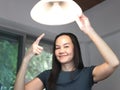 Asian woman  changing light bulb in her house, smiling, looking at camera and pointing at the lamp Royalty Free Stock Photo