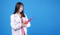Cheerful asian woman doctor in uniform with stethoscope holding clipboard over isolated blue background. Smile female medical Royalty Free Stock Photo