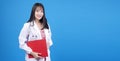 Cheerful asian woman doctor wear uniform with stethoscope holding clipboard over isolated blue background. Smile female medical Royalty Free Stock Photo
