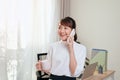 Cheerful Asian woman having conversation on mobile phone and drining coffee at office