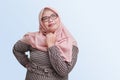 cheerful Asian woman with hijab, standing against blue background, thinking about question with hand on chin Royalty Free Stock Photo