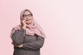 cheerful Asian woman with hijab, standing against pink background, thinking about question with hand on chin Royalty Free Stock Photo