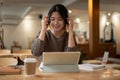 A cheerful Asian woman listening to music, and using her tablet while working remotely at a cafe Royalty Free Stock Photo