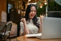 A cheerful Asian woman is looking at her laptop screen, rejoicing and celebrating her success Royalty Free Stock Photo