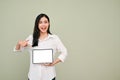 Cheerful Asian woman pointing finger at a tablet screen, standing over grey background Royalty Free Stock Photo