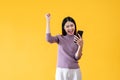 A cheerful Asian woman is showing clenched fist and looking at her smartphone with a happy face Royalty Free Stock Photo