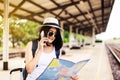 Cheerful asian woman tourist using mobile phone and looking map while waiting train at train station,Happy and smiling,Travel and Royalty Free Stock Photo