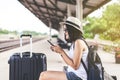 Cheerful asian woman tourist using mobile phone while waiting train at train station,Happy and smiling,Travel and vacation concept Royalty Free Stock Photo