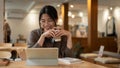 A cheerful Asian woman is working remotely at a cafe, using her tablet while enjoying her coffee Royalty Free Stock Photo