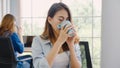 Cheerful asian young businesswoman sitting in office drinking coffee. Attractive asian creative woman holding a cup of coffee Royalty Free Stock Photo