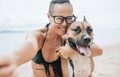 Cheerful asian young woman in eyeglases sitting and doing sekfie with her dog on the beach Royalty Free Stock Photo