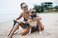 Cheerful asian young woman in eyeglases sitting and hugging her dog on the beach Royalty Free Stock Photo