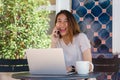 Cheerful asian young woman sitting in cafe drinking coffee and using smartphone for talking, reading and texting. Royalty Free Stock Photo