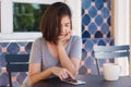 Cheerful asian young woman sitting in cafe drinking coffee and using smartphone for talking, reading and texting. Royalty Free Stock Photo