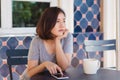 Cheerful asian young woman sitting in cafe drinking coffee and using smartphone for talking, reading and texting. Royalty Free Stock Photo