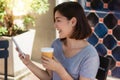 Cheerful asian young woman sitting in cafe drinking coffee and using smartphone for talking, reading and texting. Royalty Free Stock Photo