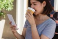 Cheerful asian young woman sitting in cafe drinking coffee and using smartphone for talking, reading and texting. Royalty Free Stock Photo