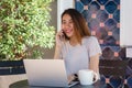 Cheerful asian young woman sitting in cafe drinking coffee and using smartphone for talking, reading and texting. Royalty Free Stock Photo