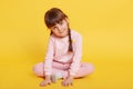 Cheerful attractive little girl sitting on floor with crossed legs, touching floor with palms, looking at camera, posing isolated Royalty Free Stock Photo