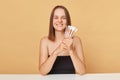 Cheerful attractive positive young brown haired woman wearing black top with makeup brushes in hand posing  over beige Royalty Free Stock Photo