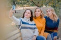 Cheerful attractive three young women best friends having fun and make selfie together outside.