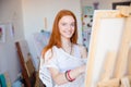 Cheerful attractive woman artist painting on canvas in art workshop