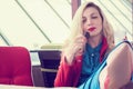 Cheerful attractive young blonde woman with long curly hair sitting in cafe with feet on the table and eating cookies. Royalty Free Stock Photo