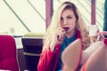 Cheerful attractive young blonde woman with long curly hair sitting in cafe with feet on the table and eating cookies. Royalty Free Stock Photo