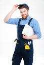 Cheerful attractive young builder in overall and cap holding laptop Royalty Free Stock Photo