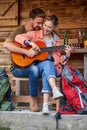 Cheerful attractive young couple enjoying vacation day and playing guitar in front of wooden cabin. Beuatiful moments. Vacation,