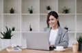 Cheerful attractive young female graphic designer smiling and working on laptop computer at her desk in modern office Royalty Free Stock Photo