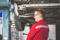 Cheerful auto mechanic working in garage, Technician man working in auto service with lifted vehicle