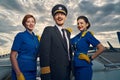 Cheerful aviator and flight attendants standing on the boarding stairs