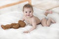 Cheerful baby boy girl in a diaper lying with a teddy bear. Cute baby in a diaper crawling on the bed, look into the camera Royalty Free Stock Photo