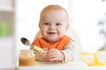 Cheerful baby child eats food itself with spoon. Portrait of happy kid boy in high-chair. Royalty Free Stock Photo