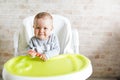 Cheerful baby child eats food itself with spoon. Portrait of happy kid in high chair in sunny kitchen. background with copy space Royalty Free Stock Photo