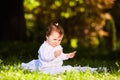 Cheerful baby girl sitting on the green grass in the city park at summer day. Royalty Free Stock Photo