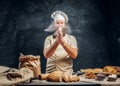 Cheerful baker claps his hands with flour over the table with freshly prepared products from his bakery