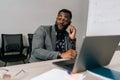 Cheerful bearded African businessman in suit talking on smartphone sitting at office desk with laptop. Happy confident Royalty Free Stock Photo