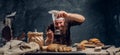 Cheerful bearded baker sprinkling some flour on his freshly made muffin next to a table