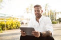 Cheerful bearded businessman reading news on digital tablet, sitting outdoors near office during break, free space Royalty Free Stock Photo