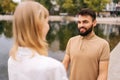 Cheerful bearded man standing holding hands with girlfriend outdoors by beautiful lake at city park, talking and looking Royalty Free Stock Photo