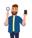 Cheerful bearded young man holding magnifying glass and mobile, cell, smart phone in hand. Search, find, discovery, analyze.