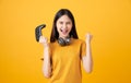 Cheerful beautiful Asian woman in casual yellow t-shirt and playing video games using joysticks with headphones.