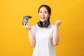 Cheerful beautiful Asian woman in casual yellow t-shirt and playing video games using joysticks with headphones.