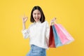 Cheerful beautiful Asian woman holding multi coloured shopping bags and shows ok sign on light yellow background. Royalty Free Stock Photo